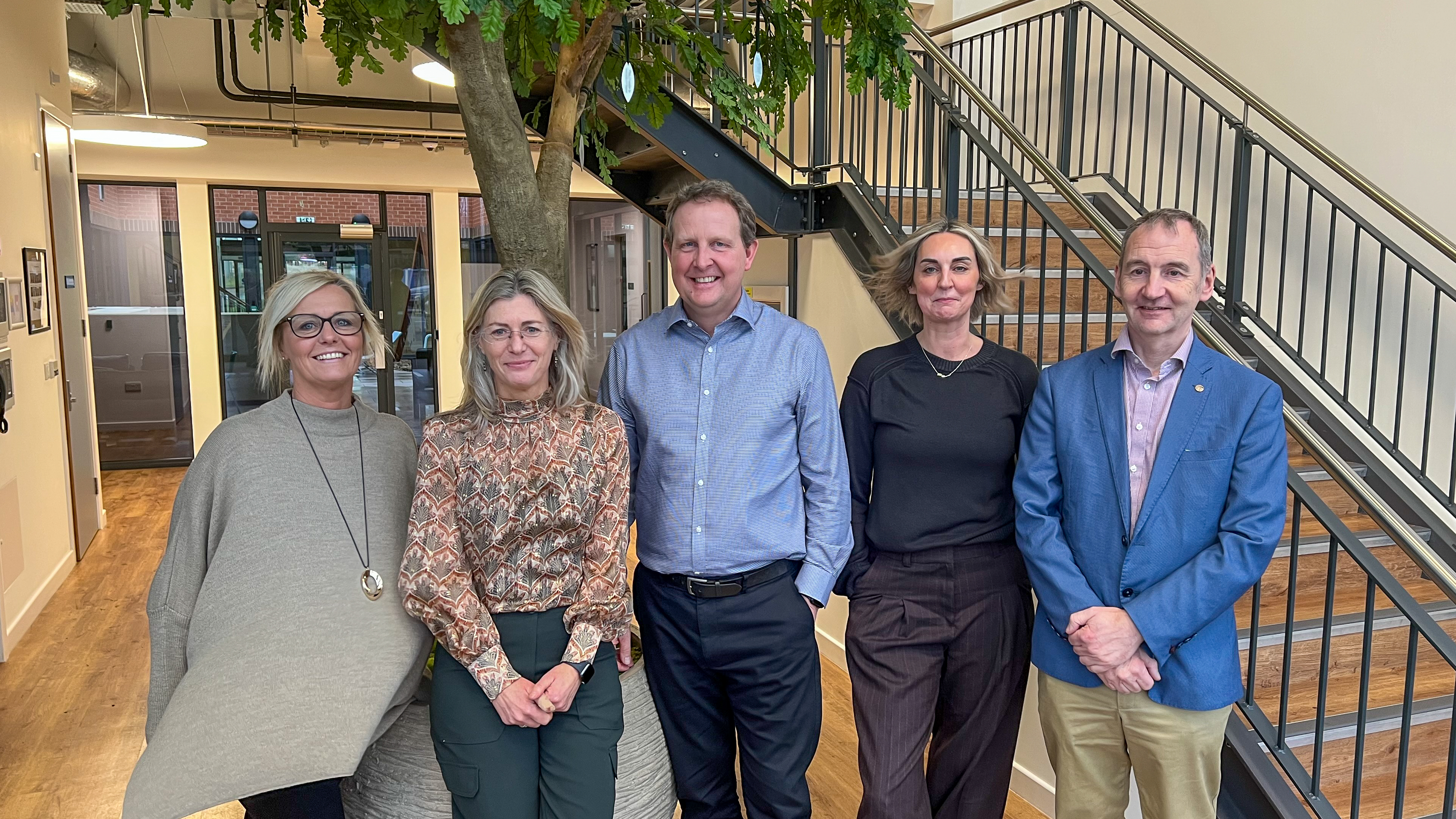 A group of five people in smart business wear in front of a tree