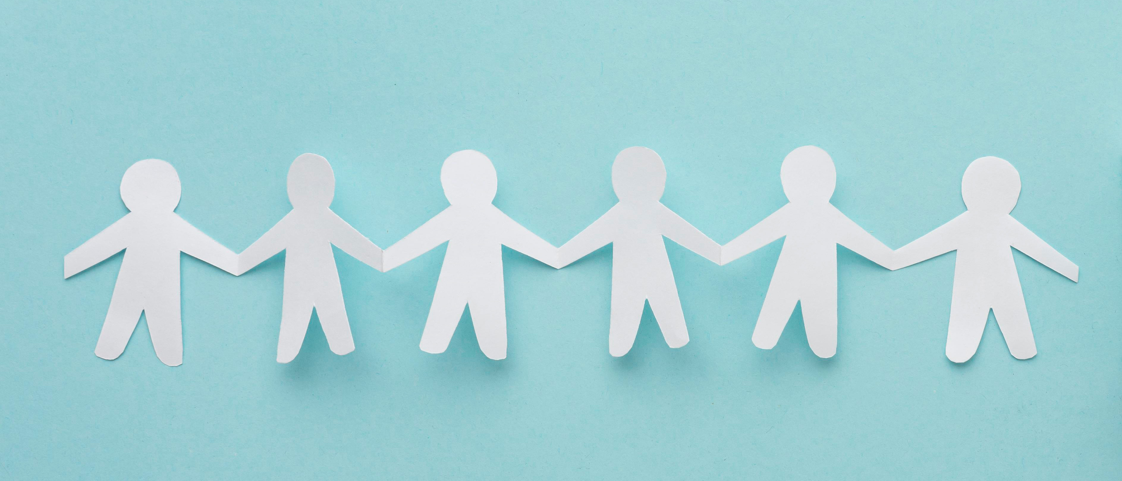 Photo of a paper chain shaped like a row of people cut out of white paper lying on a turquoise surface