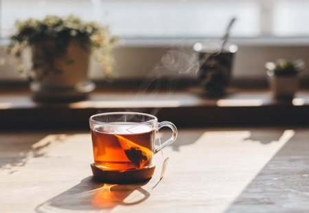A cup of tea in a glass mug sitting in autumn sunshine