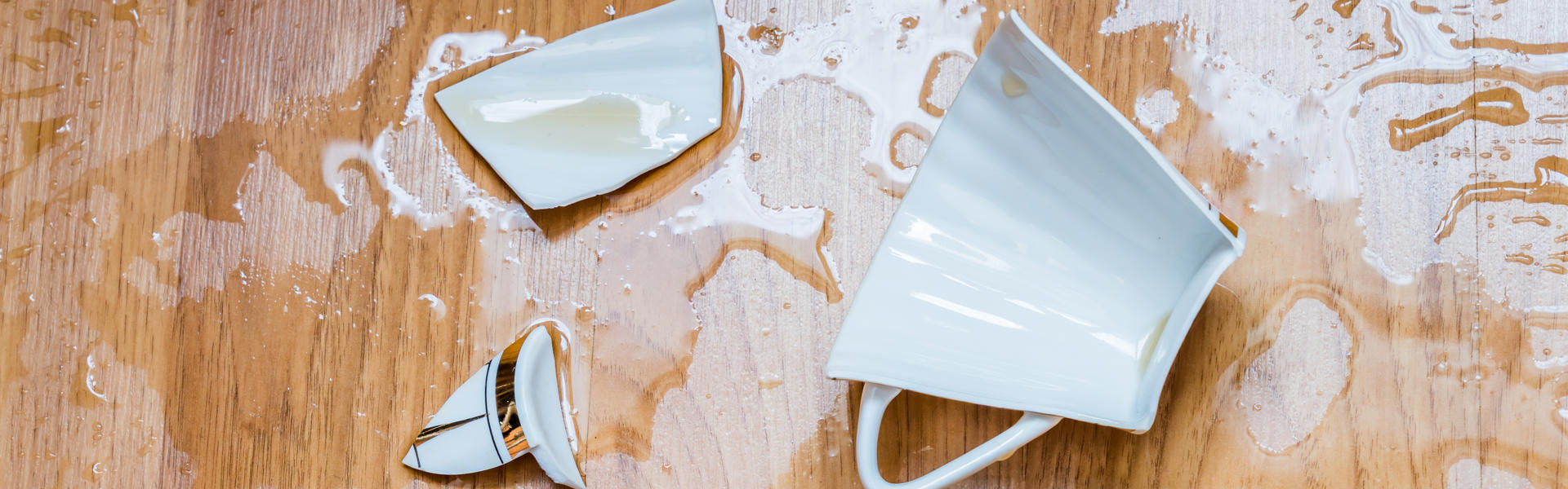 A broken tea cup on a wooden floor.