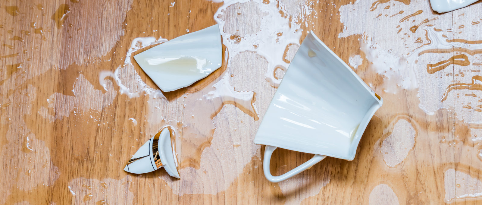 A broken tea cup on a wooden floor.