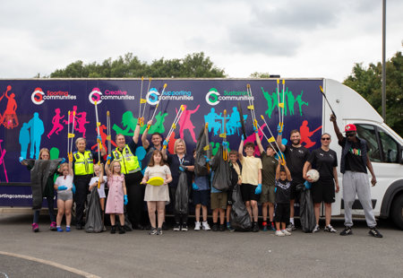 Group of partners and children with litter pickers and sports equipment