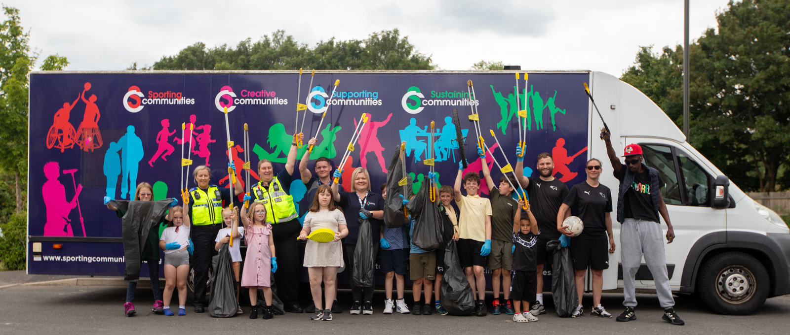 Group of partners and children with litter pickers and sports equipment