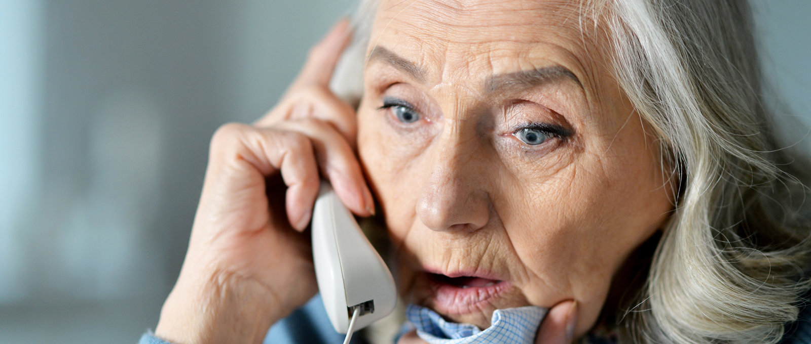 Close up photograph of the face of an older woman on the phone and looking stressed or shocked