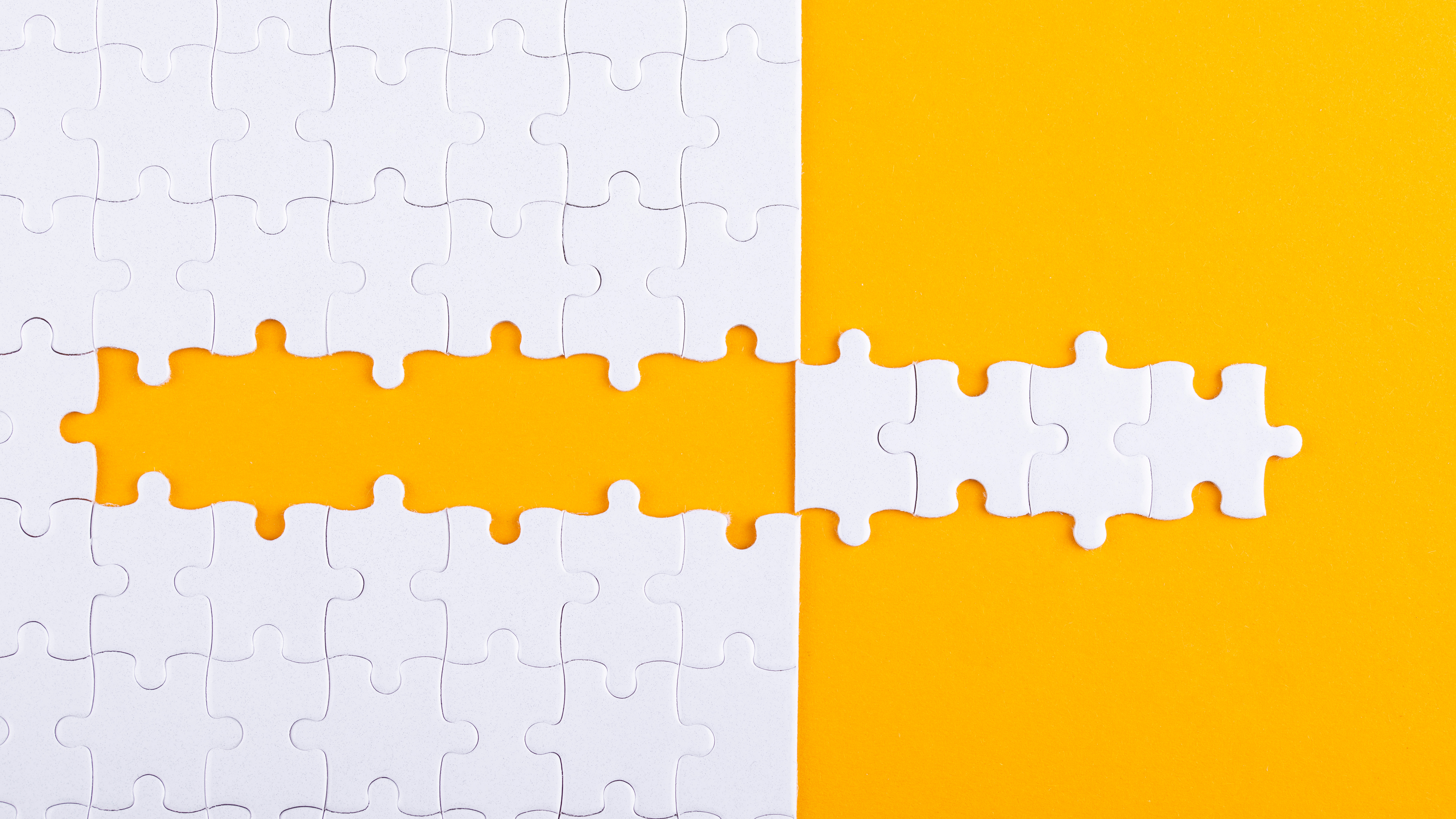 Photo of white jigsaw pieces on an orange surface. Several pieces have been removed from the puzzle in a strip and placed to the side of the jigsaw to create a 'mirror image' effect