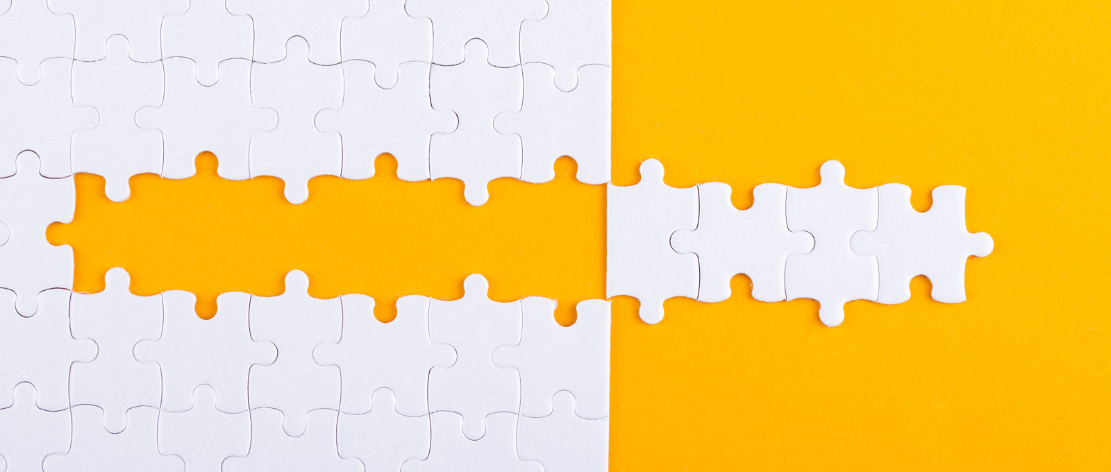 Photo of white jigsaw pieces on an orange surface. Several pieces have been removed from the puzzle in a strip and placed to the side of the jigsaw to create a 'mirror image' effect