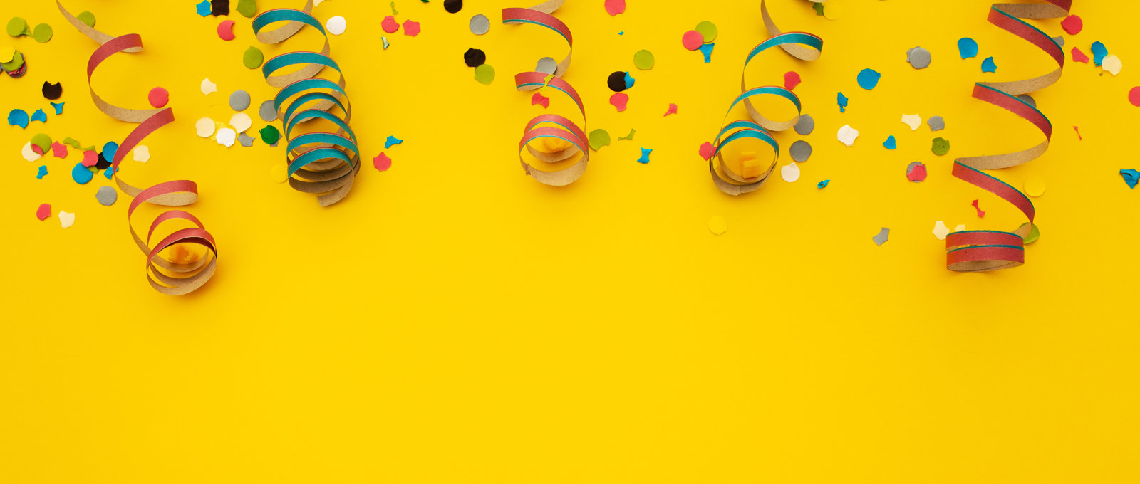 Different coloured spiralling steamers and paper confetti on a yellow surface