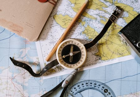 A compass and pencil lying on top of various maps