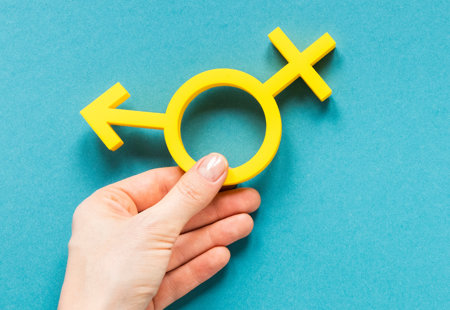 Close-up of a hand holding a yellow hybrid symbol of male and female gender symbols. 