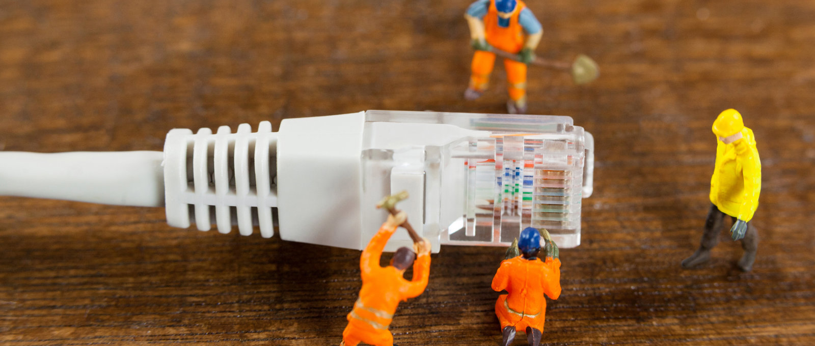 Super close up photo of a computer ethernet plug with four tiny models of 'engineers' working around it