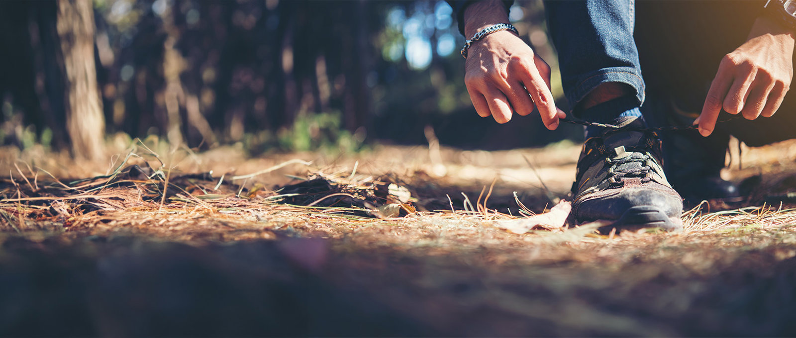 Man Tying Up Walking Shoes In A Forest Banner