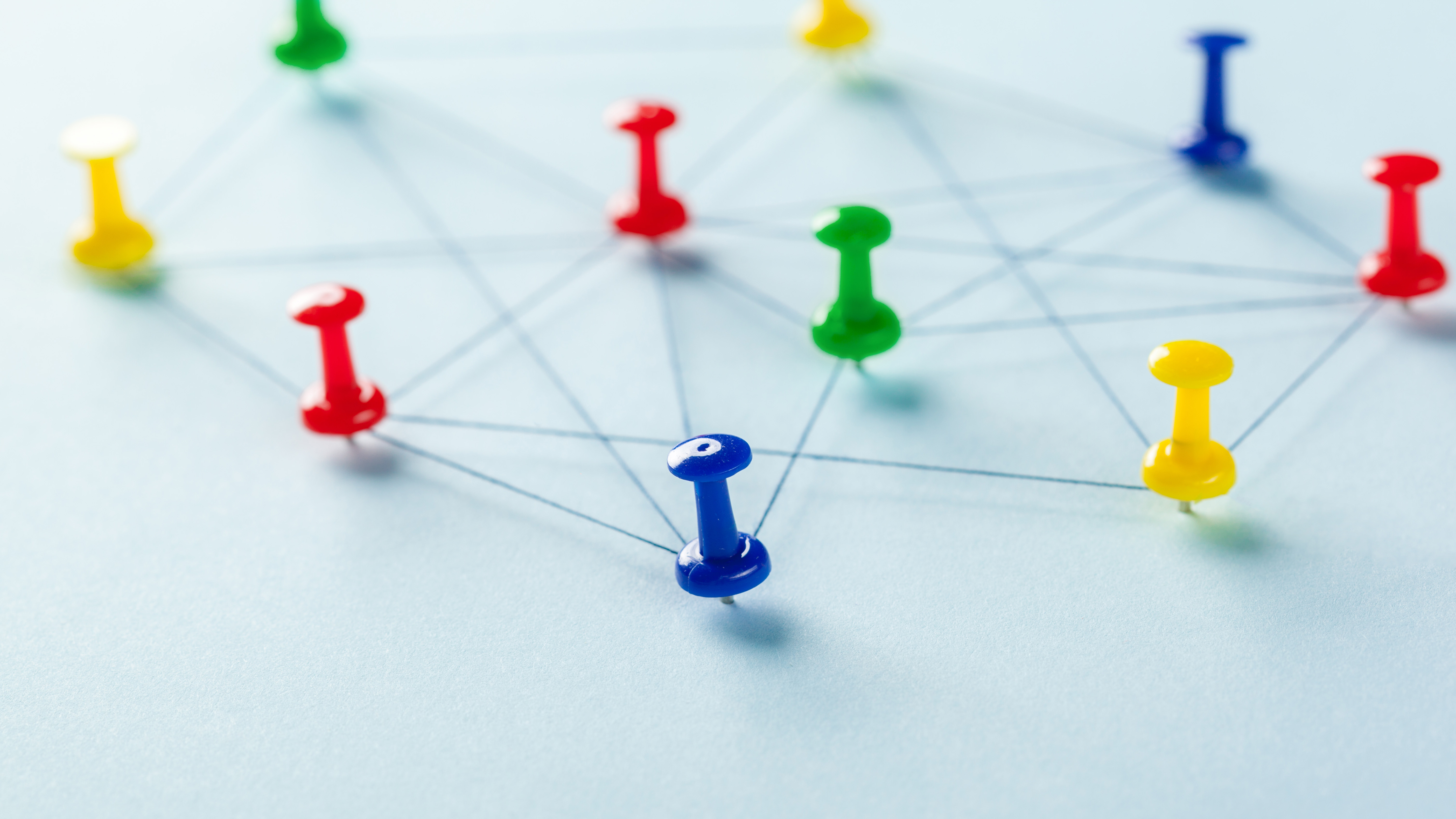 Photo of various coloured pins stuck into a light blue surface, interconnected by lines of thread