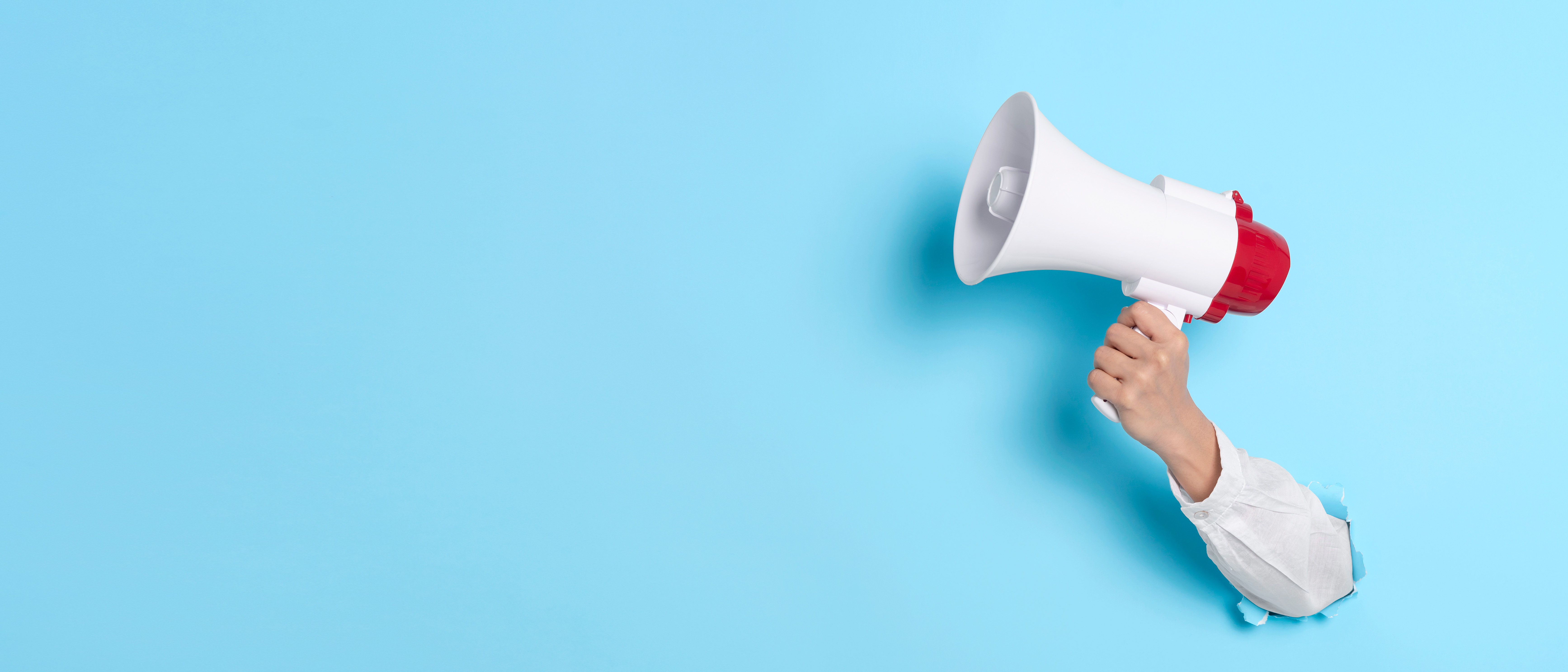 photo of a hand pushed through the light blue background and holding a white and red megaphone