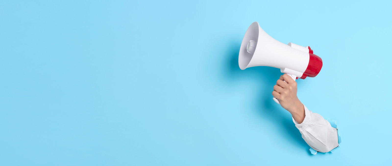 photo of a hand pushed through the light blue background and holding a white and red megaphone