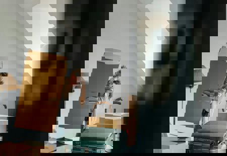 Photo of a woman lifting a large carboard box in what looks like a bedroom. There are other boxes and a suitcase visible