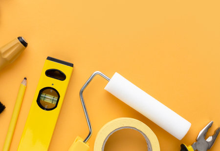 Close-up of various household DIY tools. Spirit level, paint roller, screw driver, masking tape arranged on a yellow surface
