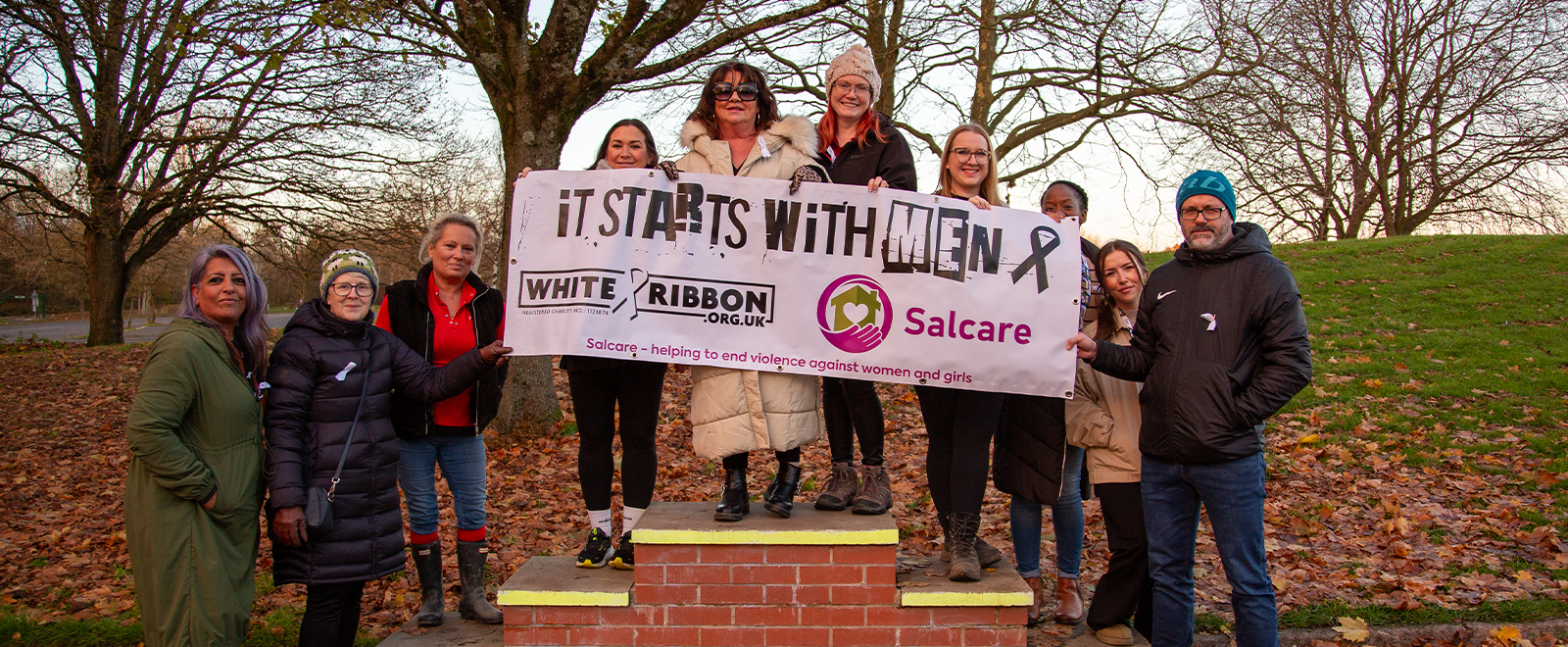 Photo of a group of people holding a banner that says 'It starts with Men - White Ribbon Day - Salcare'