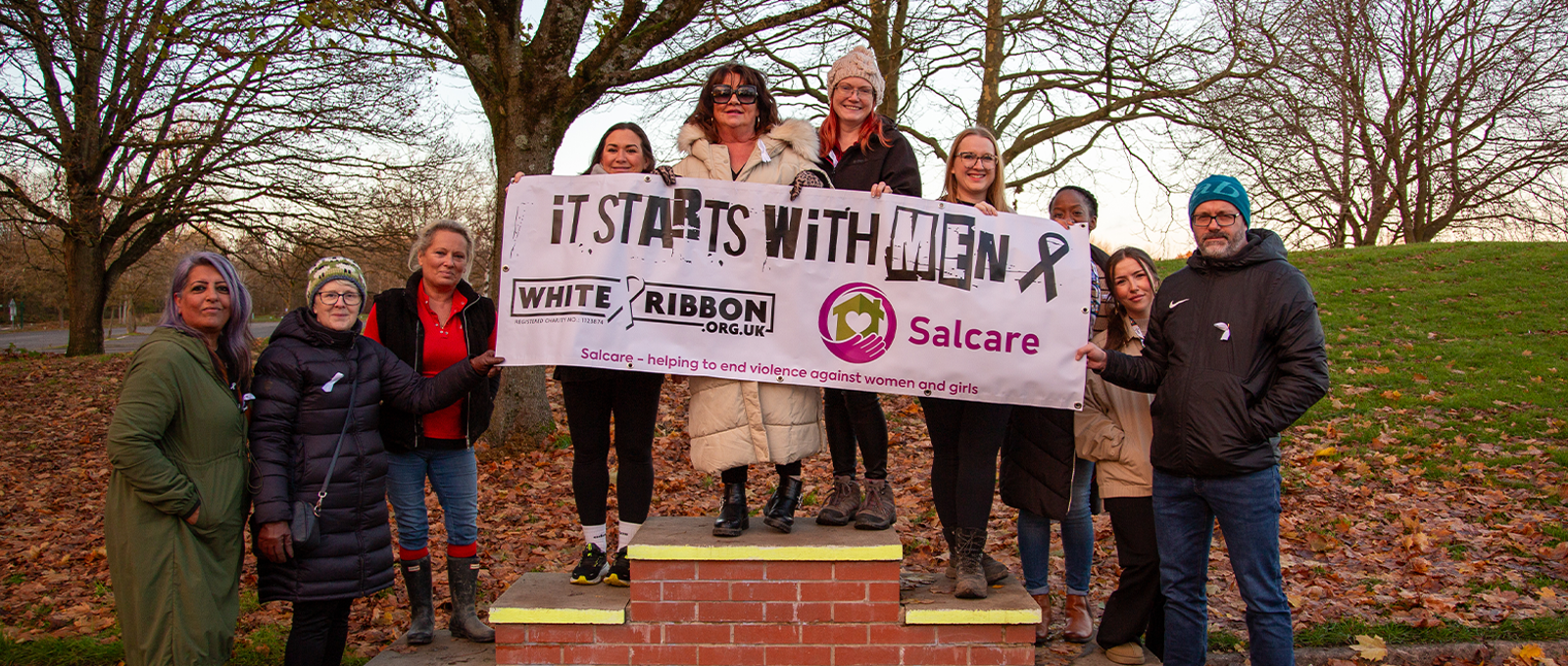 Photo of a group of people holding a banner that says 'It starts with Men - White Ribbon Day - Salcare'