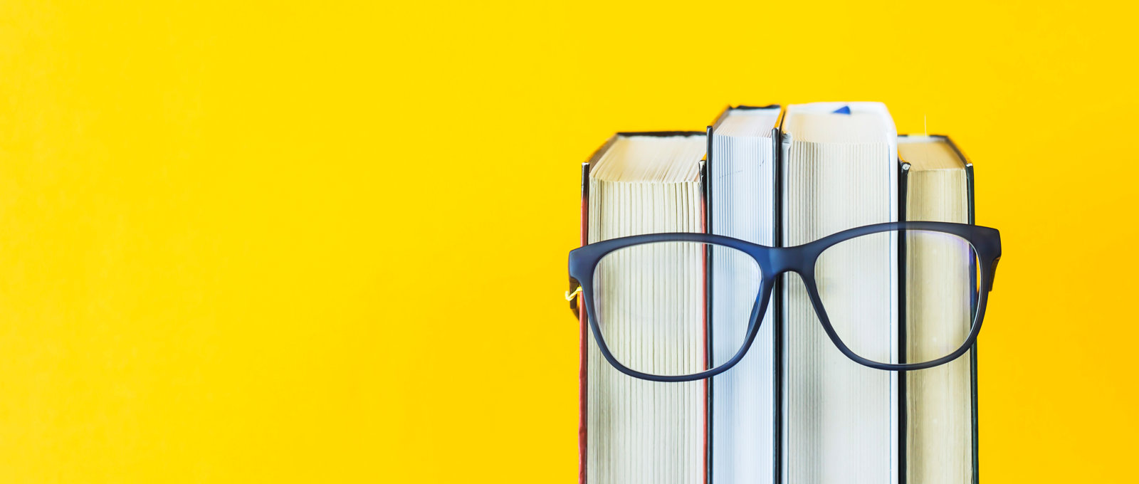 Photo of a pair of glasses resting on some books against a yellow background