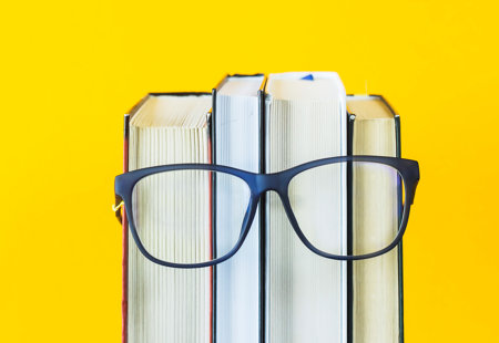 Photo of a pair of glasses resting on some books against a yellow background