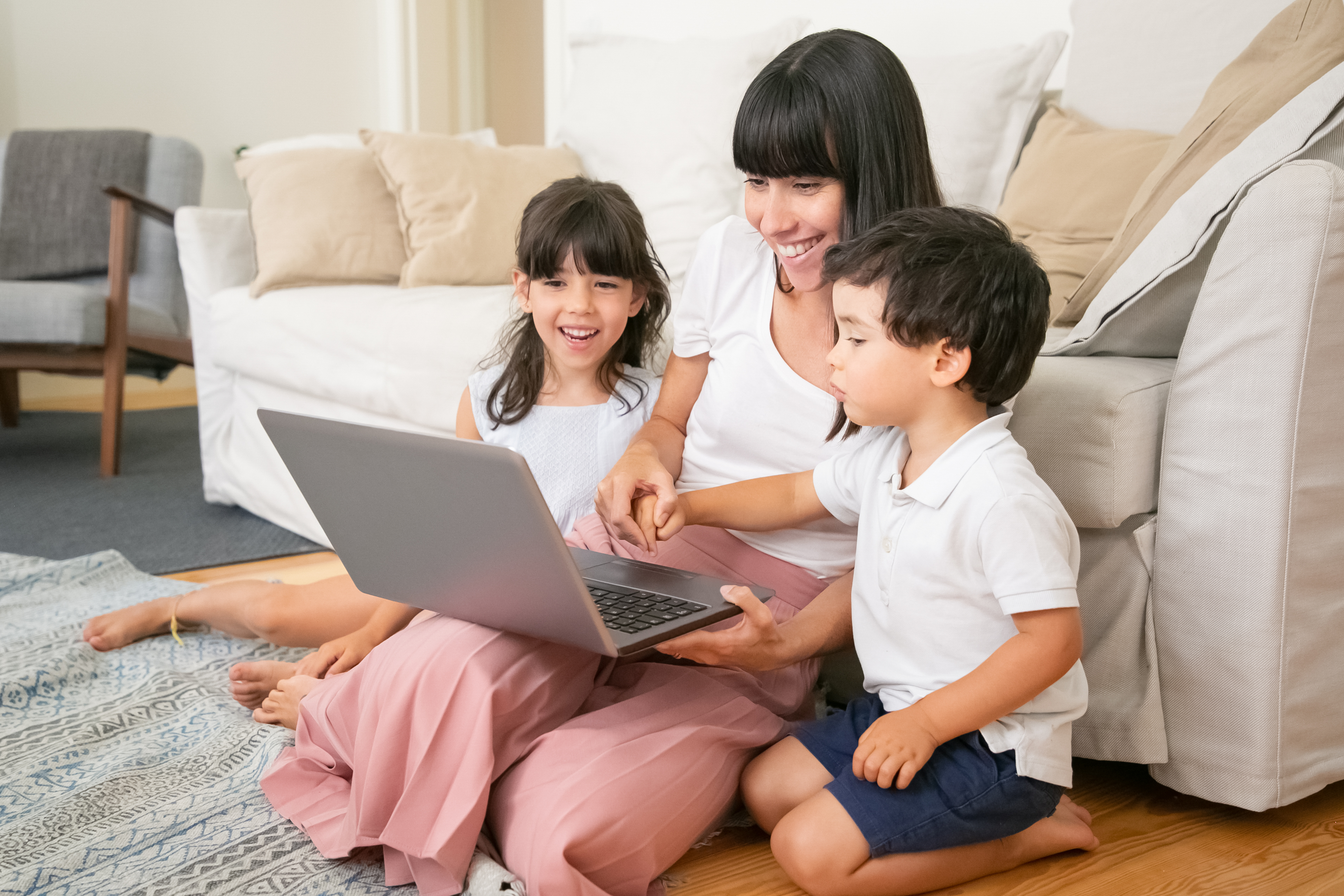 Mum with two children sat on the floor, all happy looking at a laptop