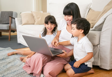 Mum with two children sat on the floor, all happy looking at a laptop