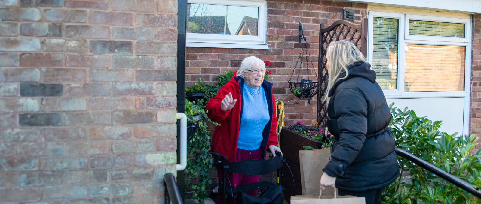 young woman carrying brown paper bag talking with old woman outside a property
