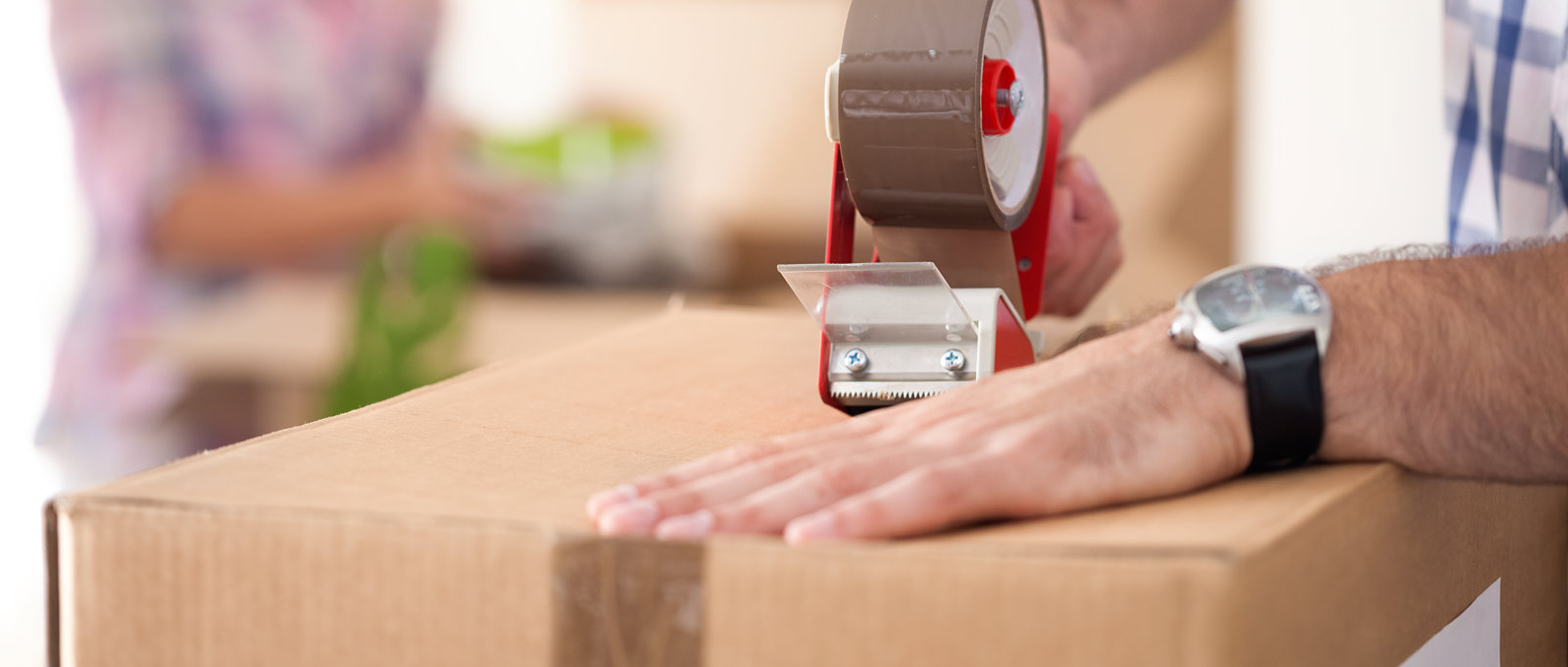 Close up photograph of a man sealing up a packing box with tape.