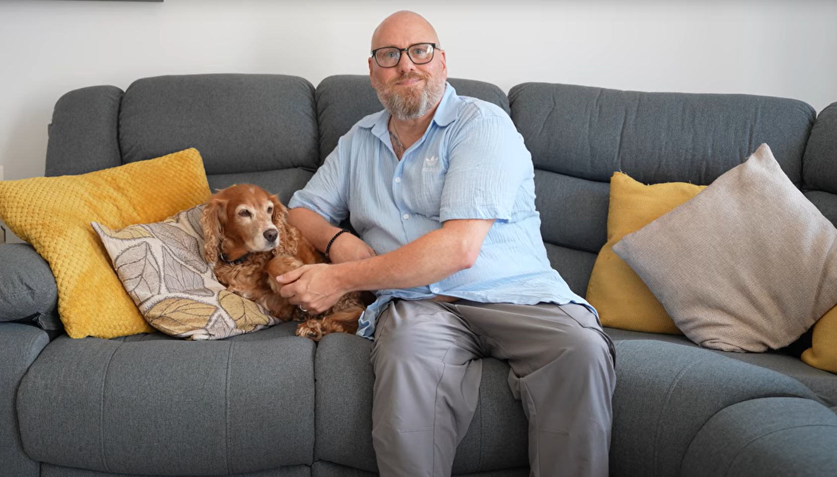 Simon sits with his dog Sandy on a grey sofa