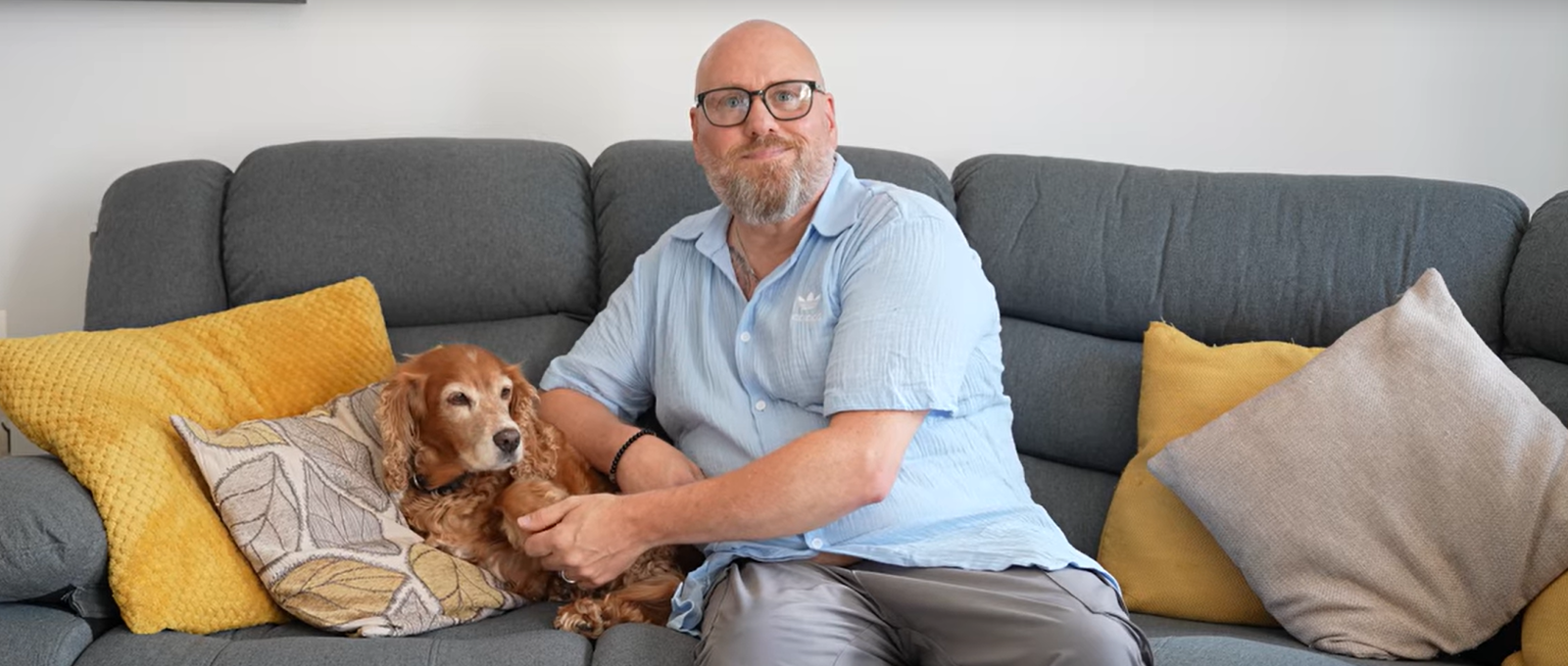 Simon sits with his dog Sandy on a grey sofa