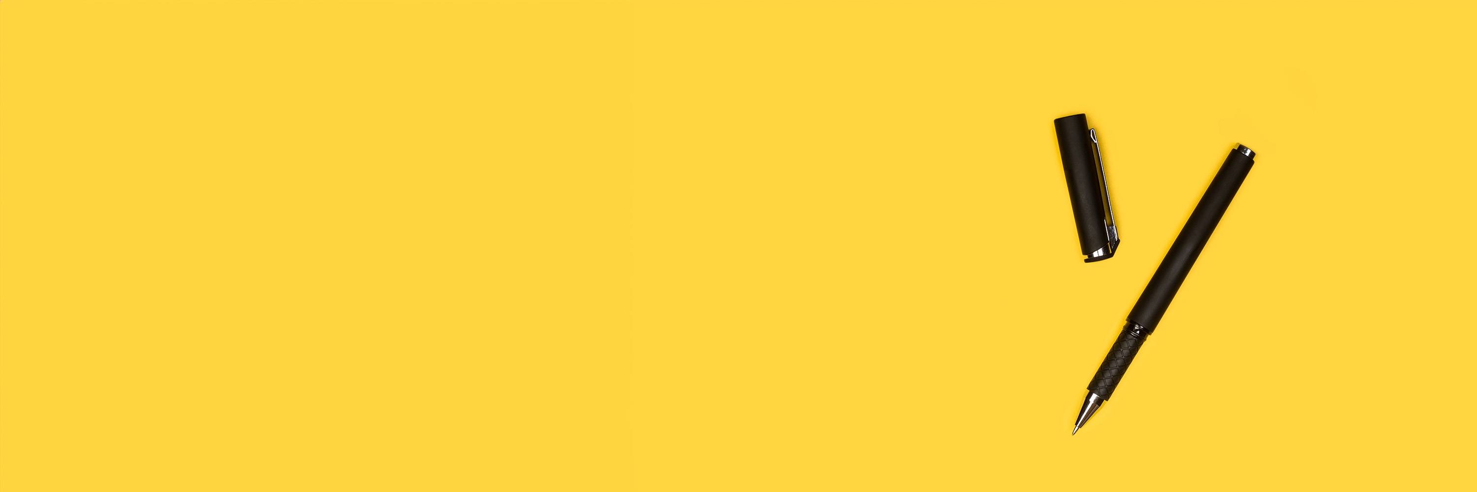 Photo of a black pen with the lid removed lying on a yellow surface