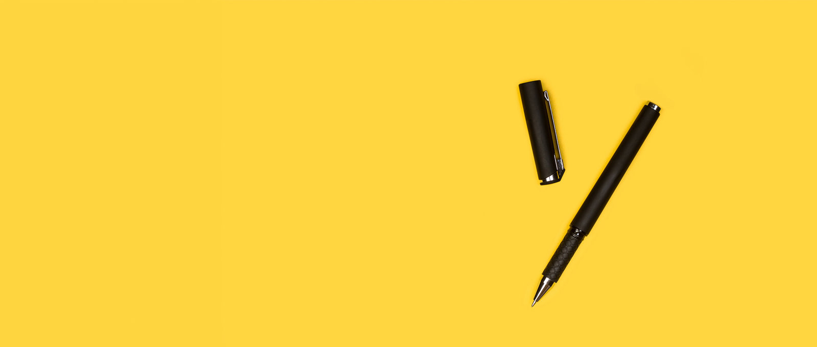 Photo of a black pen with the lid removed lying on a yellow surface