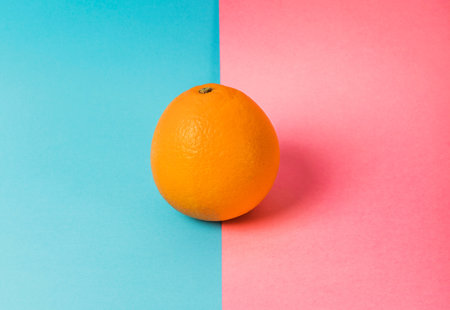 Photo of an orange on a background that if half turquoise and half pink. The orange sits on the dividing line.